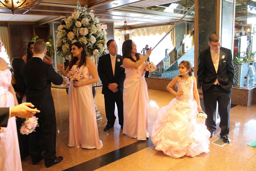 Wedding party posing indoors, light pink dresses and black suits. Flower girl in ornate gown.