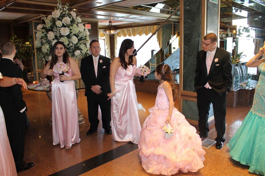 Wedding party in formal attire indoors. Light pink gowns and black suits, flower bouquet, and a flower girl.