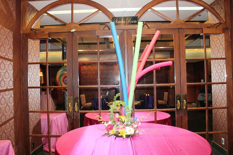 Pink table with floral centerpiece and colorful decorations, in front of glass doors.