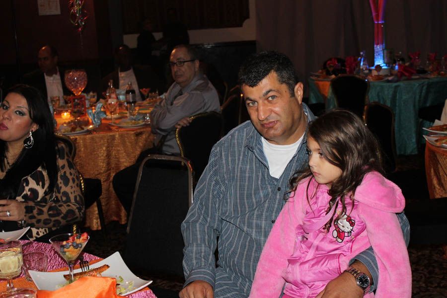 Man holding girl at a table, people in background at a celebration.