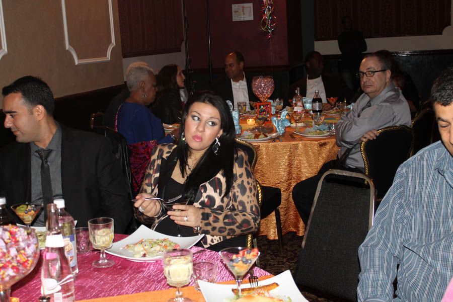 People seated at tables in a restaurant, a woman in a leopard-print jacket is the central focus.