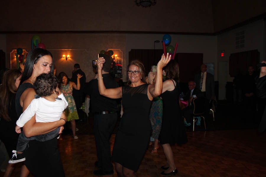 People dancing at a celebration in a dim room with balloons; several in black dresses.