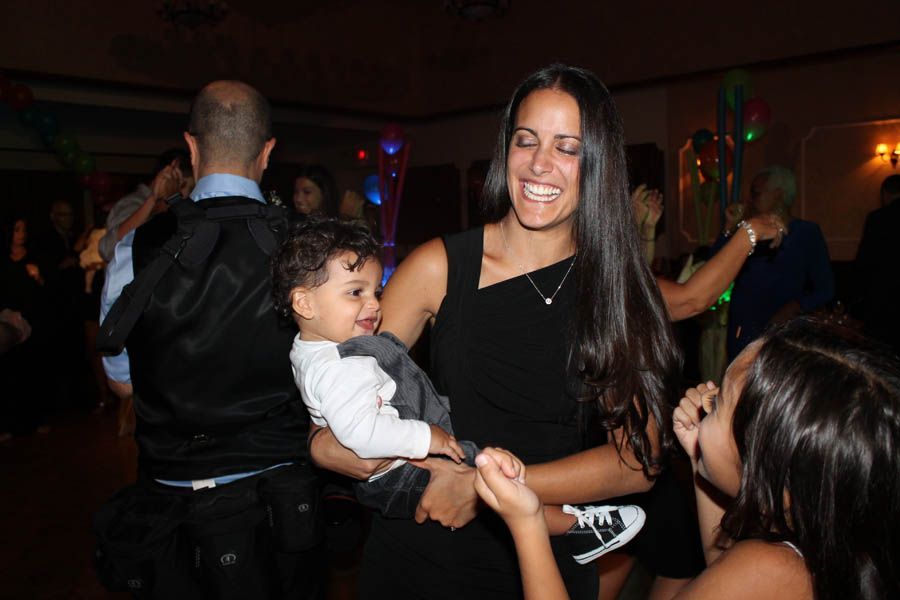 Woman dancing with child; laughing, black dress, other people in background at party.