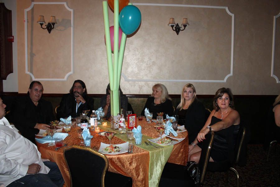 People seated around a decorated table at a party, with balloons and colorful tablecloth.