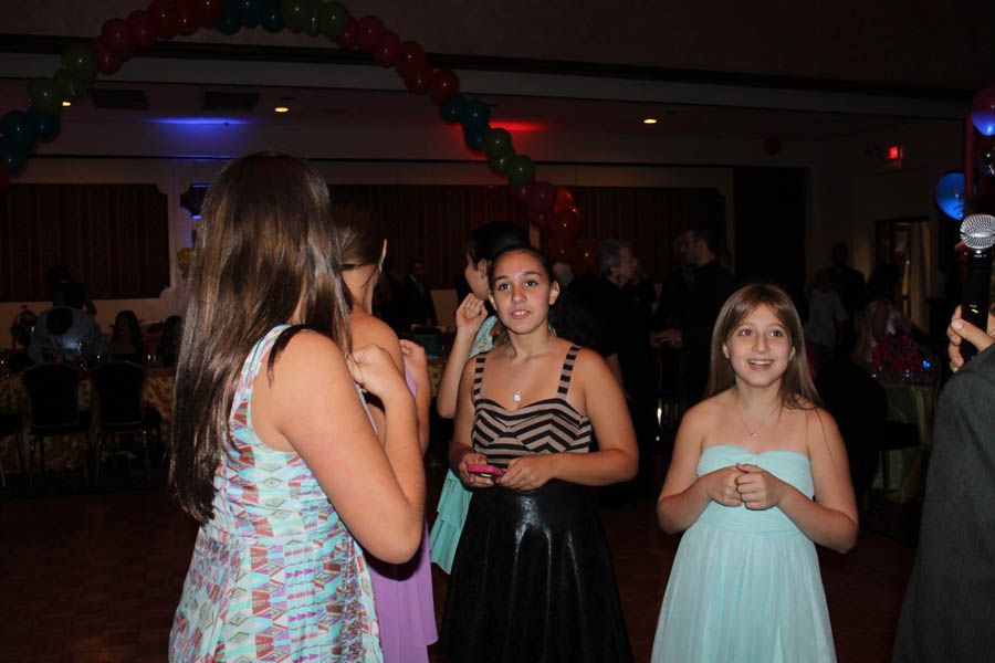 Girls in dresses at a dance with balloons and a dance floor.