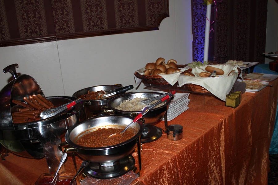 Buffet table with various dishes in metal chafing dishes and a basket of rolls.