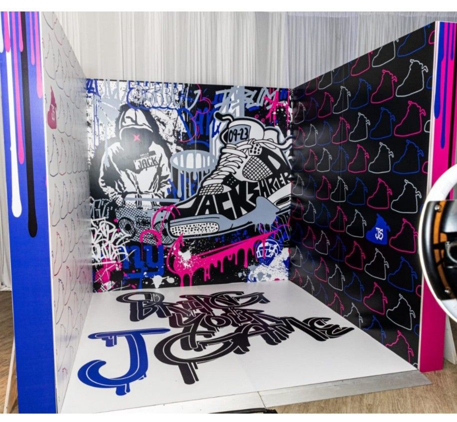 Graffiti-style display with sneaker artwork, vibrant colors, and text. White, black, and pink dominate.