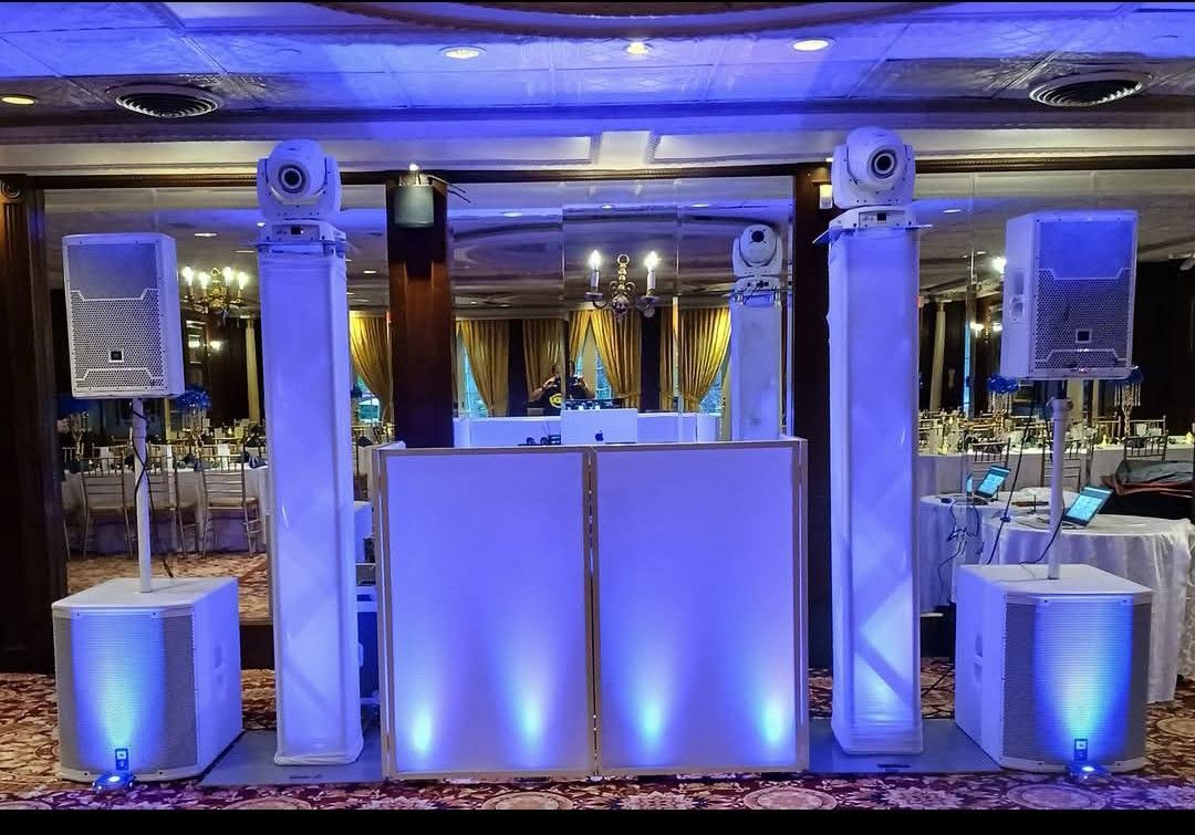 DJ setup with white pillars, speakers, and lighting. Blue and white color scheme in a banquet hall setting.