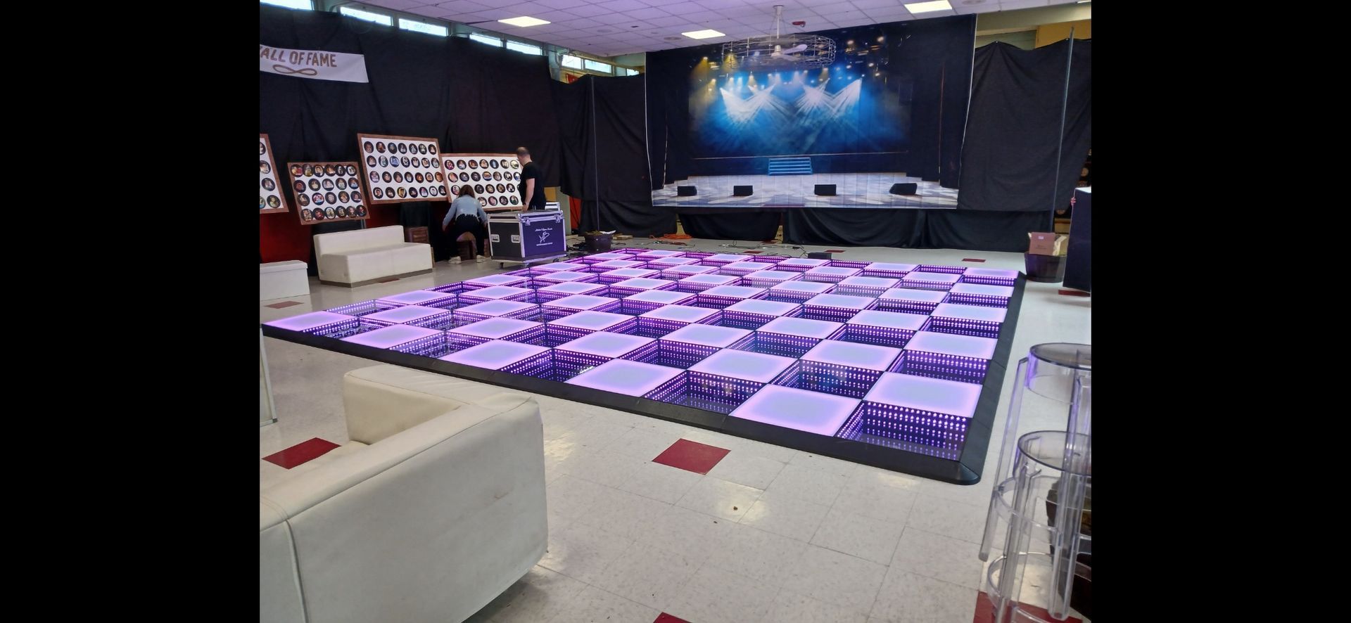 Lit-up purple checkered dance floor in a venue with a stage and seating.