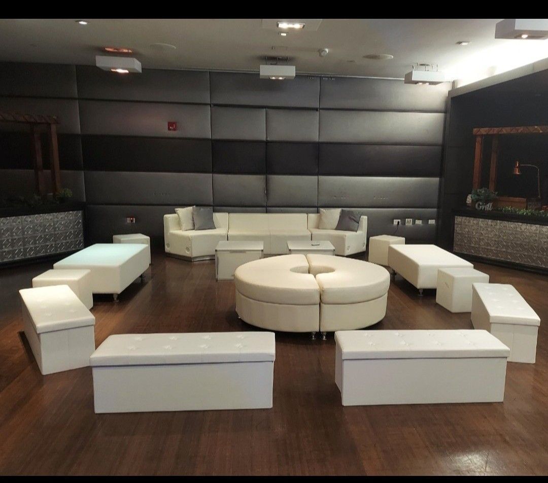 Lounge area with white modular seating on wooden floor; gray and black padded wall backdrop.