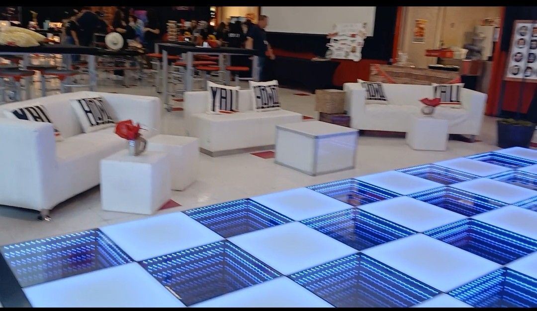 White couches with red flower centerpieces, lit checkered dance floor, event setting.