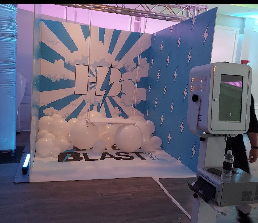 Photo booth setup with a blue and white lightning bolt themed backdrop and white balloons.