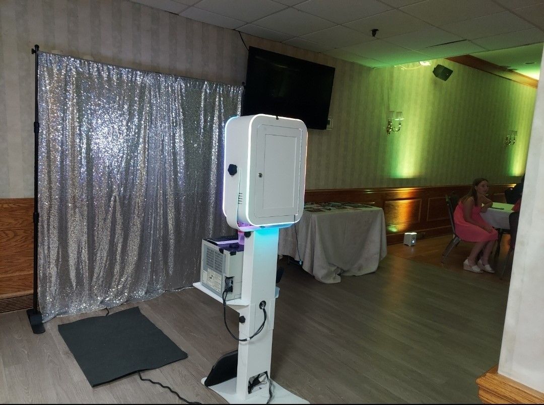 Photo booth with silver backdrop in a room with green lighting.