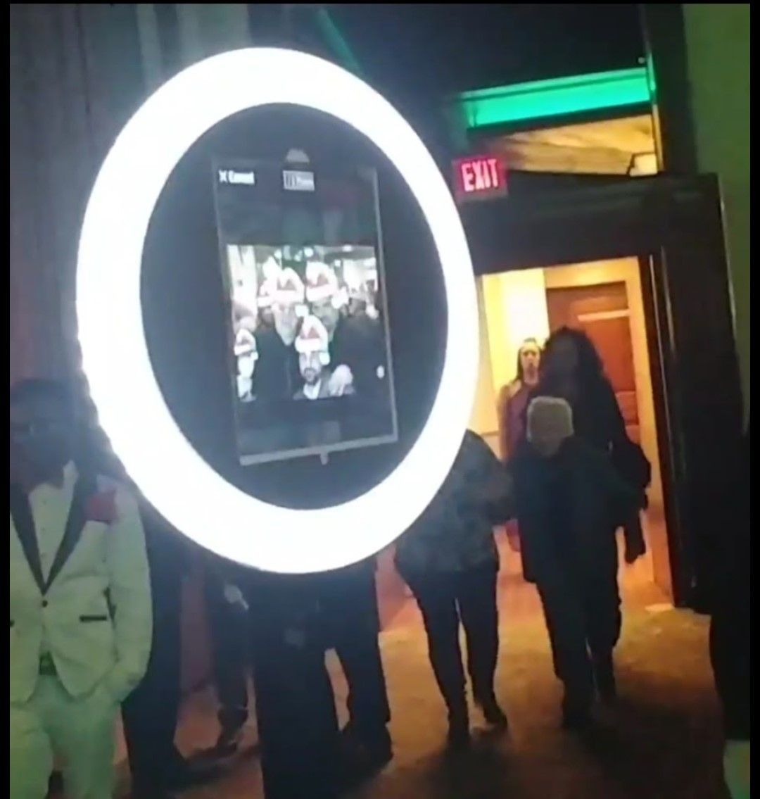 Large ring light with people walking through doorway, a photo booth in operation.