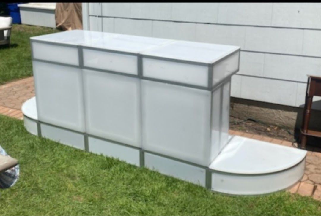 White rectangular bar with curved base, metal trim, and translucent panels, outdoors on grass.