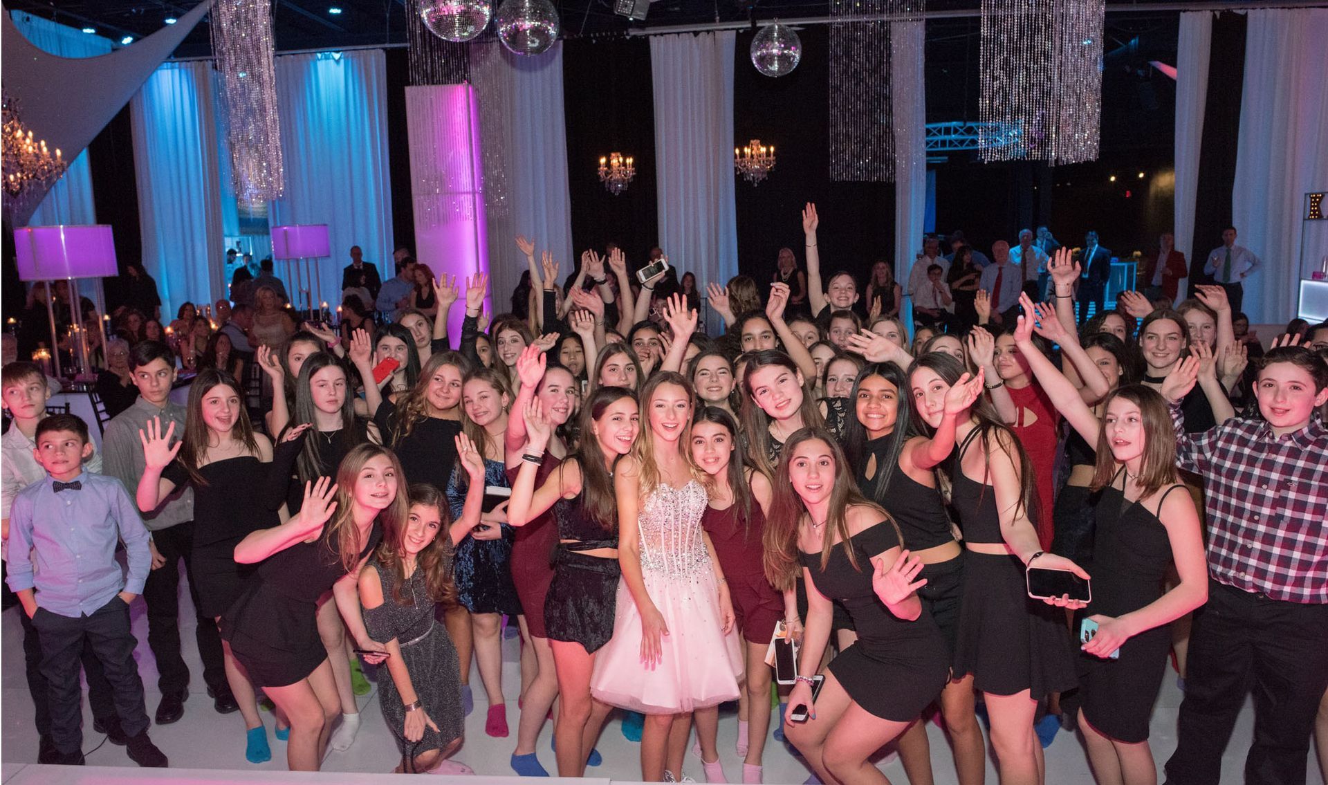 Large group of people at a party, many with arms raised, in a room with decorations and lights.
