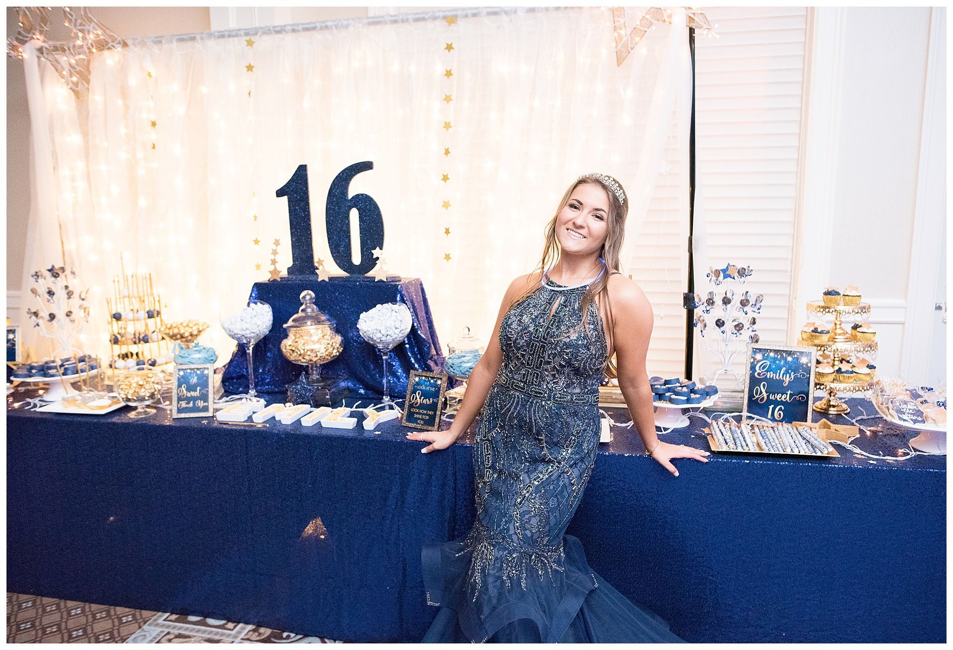 Woman in formal dress smiles at Sweet 16 party with navy and gold decorations.