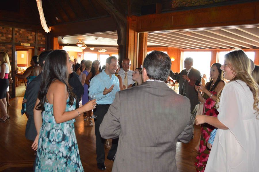 People dancing at an indoor event with wooden floors and walls. Some people hold drinks.