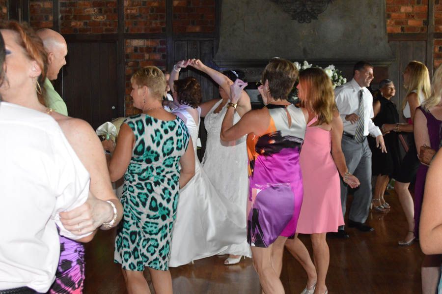 People dancing at a wedding reception. Bride in white dress, guests in colorful dresses, wooden dance floor.