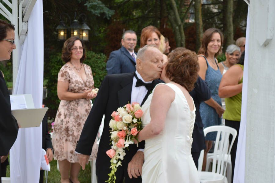 Groom kisses bride during outdoor wedding ceremony; guests watch.
