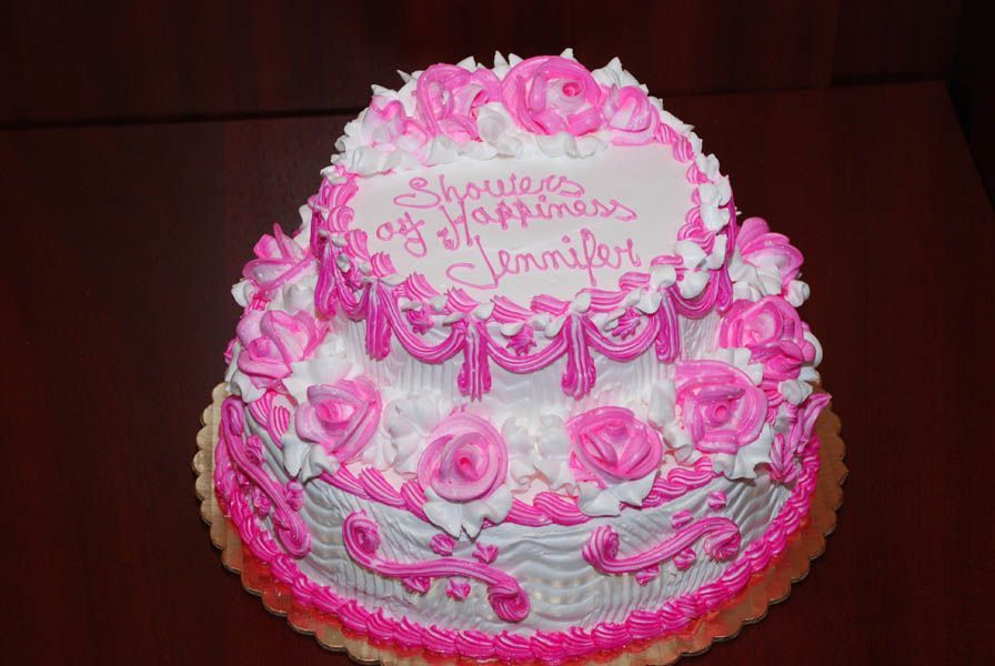 Two-tiered cake with pink and white frosting, decorated for a shower, says 