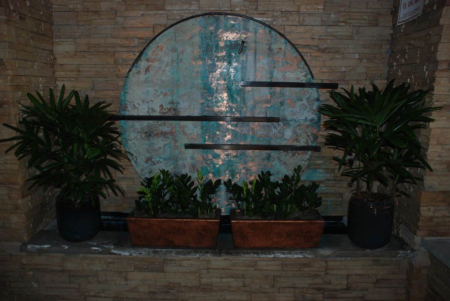 A decorative wall with a teal circle, metal bars, and potted plants on a brick ledge.