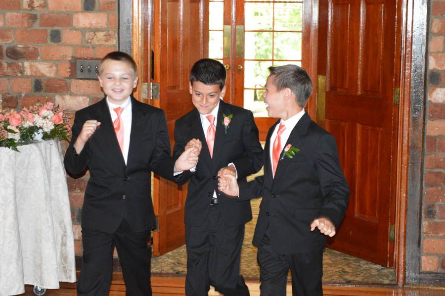 Three boys in black suits and coral ties, entering a building with a large wooden door.