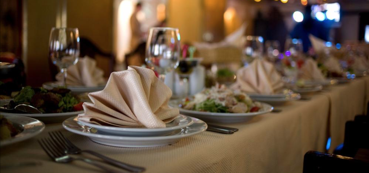 A long table set for a formal dinner at a restaurant, with plates, folded napkins, and glasses.
