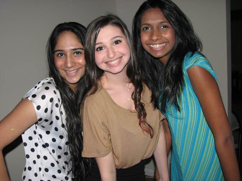 Three young women smiling, posing closely together. One in polka dots, one in beige, and one in teal.