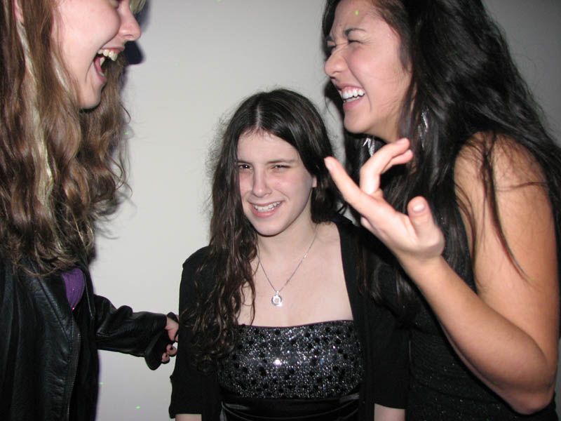 Three laughing people in a dimly lit room, two flanking one in the middle; one person gesturing.