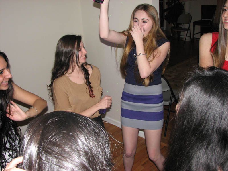 Women celebrating indoors, one holding a microphone, others smiling and dancing.