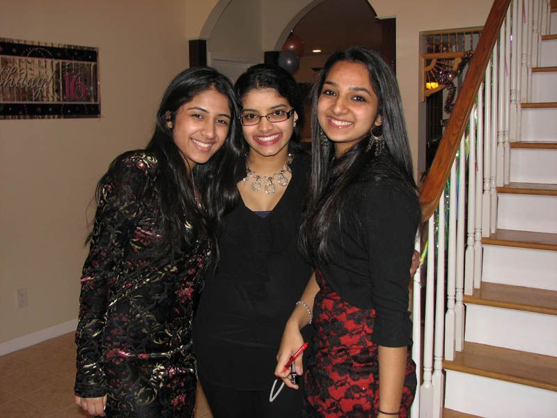 Three young women smiling, posing for a photo. Indoors with stairs in the background.