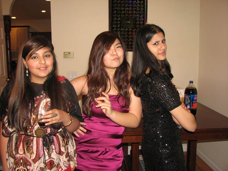 Three people posing indoors. One holds a drink, one makes a face, and the last looks back.