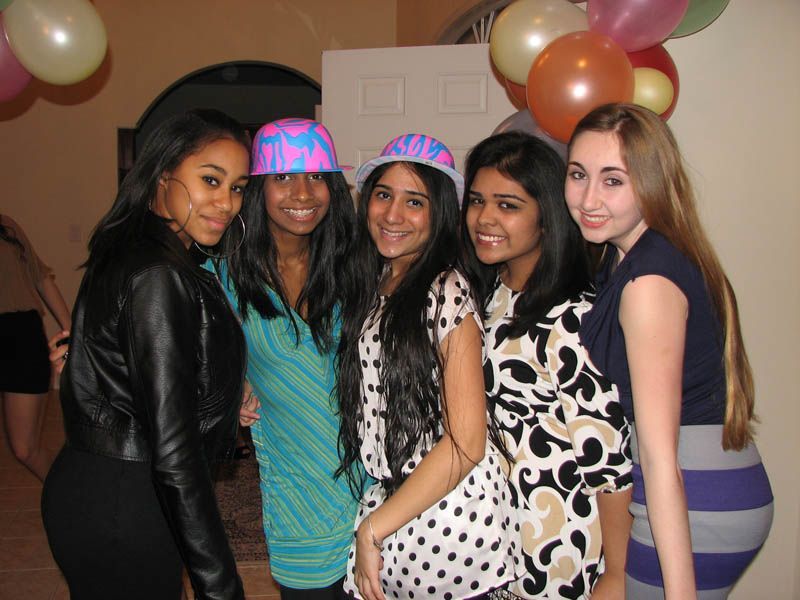 Five young people pose, smiling, with hats and balloons at a party.