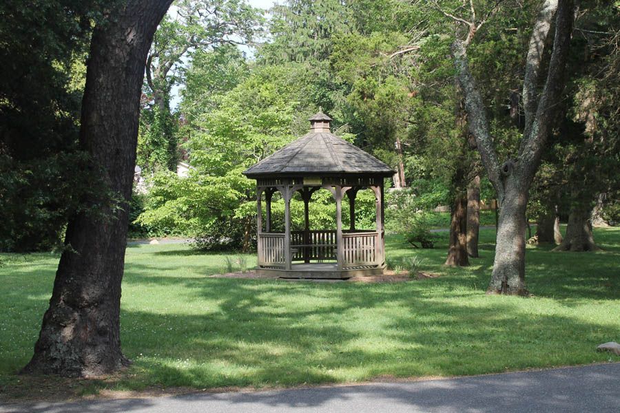 Wooden gazebo in a grassy park, surrounded by trees.