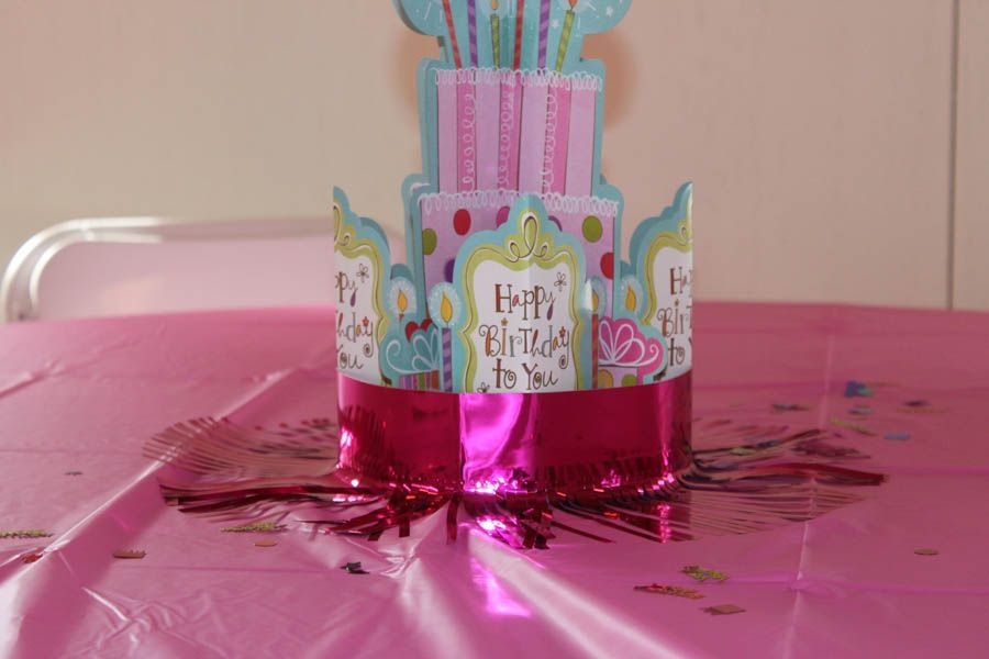 Pink birthday cake centerpiece on pink tablecloth.