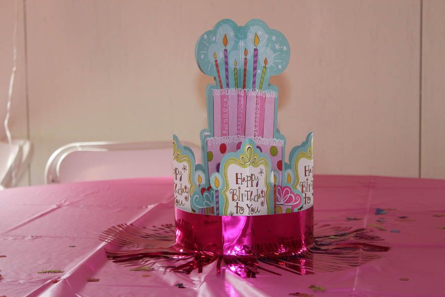 Pink and blue paper birthday cake centerpiece on a pink tablecloth with confetti.