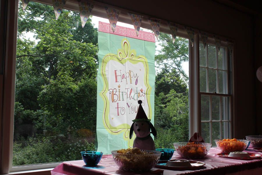 Birthday banner in a window with snacks and a plush dog.