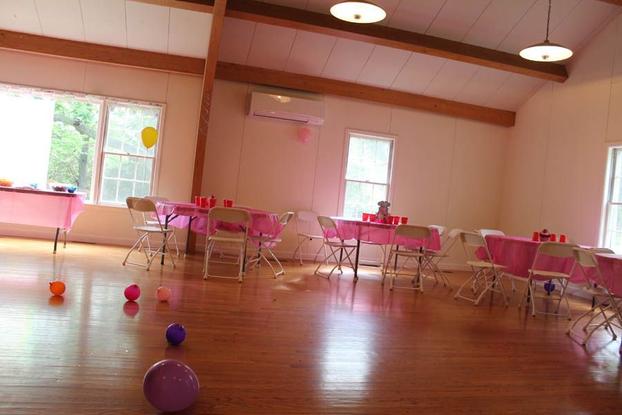 Pink party decorations in a brightly lit room with wooden floors, tables, and chairs.