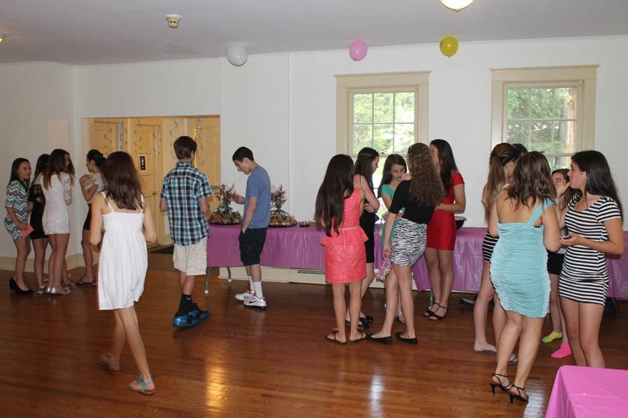 Teenagers at a party in a room with balloons, a table with food, and wood floors.