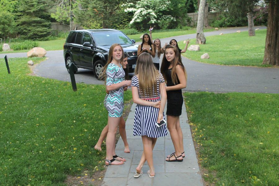 Group of people near a black SUV on a driveway; some waving.
