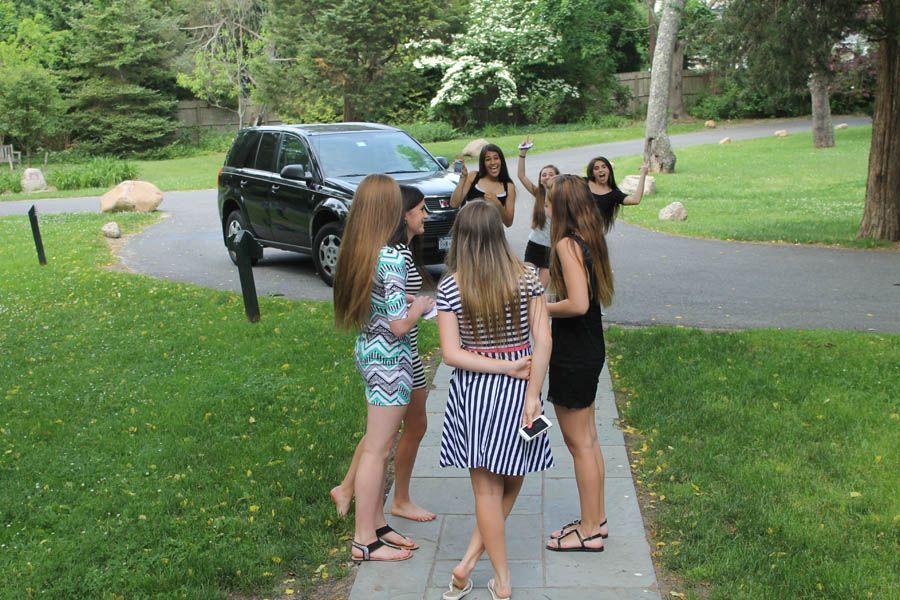 A group of girls standing on a walkway near a black SUV on a grassy lawn.