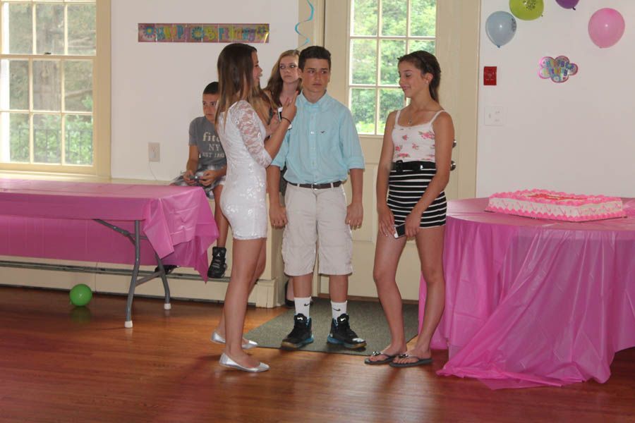 Teenagers at a party in a room, two tables covered with pink tablecloths, balloons.