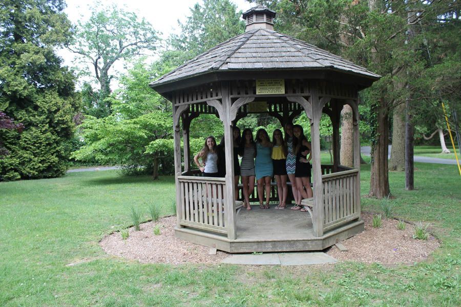 Group of people standing inside a wooden gazebo in a park-like setting.