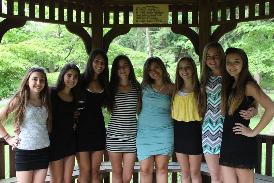 Group of eight people posing in a gazebo; some are wearing dresses and smiling, set outdoors.