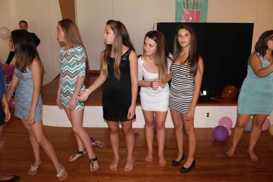 Group of young people in short dresses on a wooden floor, some barefoot, at a party with balloons.