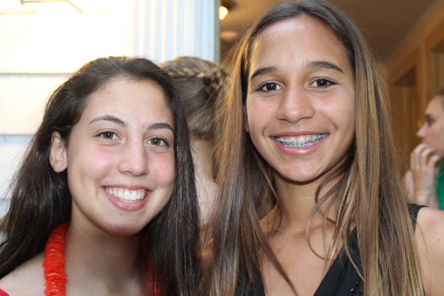 Two smiling people at an event; one with braces, the other with a lei; soft lighting.