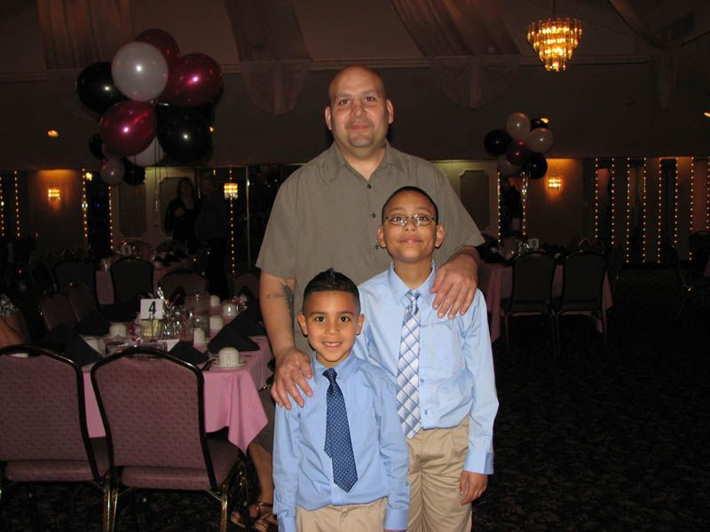 A man with two boys posing for a photo at a decorated event with balloons and tables.