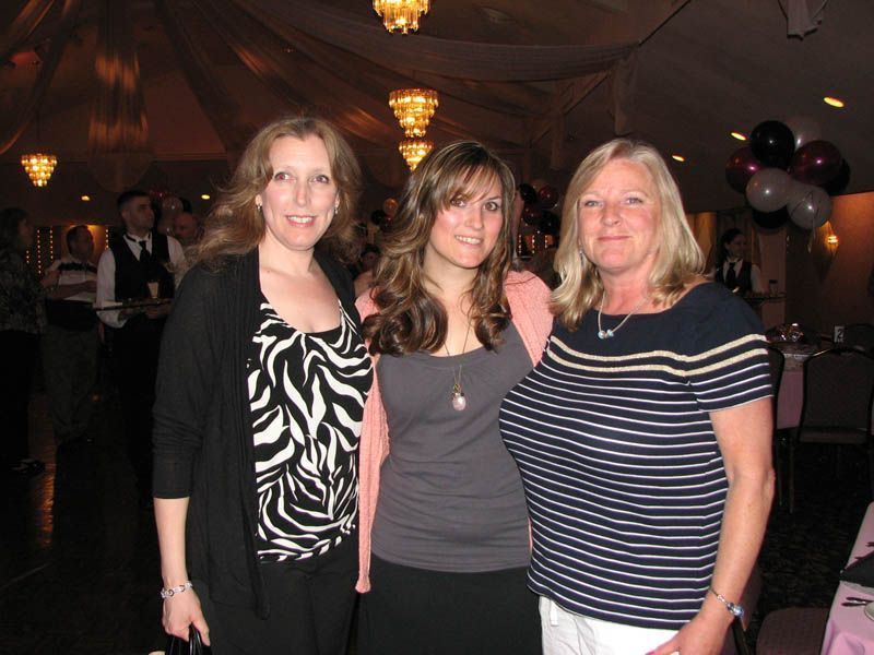 Three women posing together indoors; one in black and white patterned top, one in gray, and one in blue and white stripes.