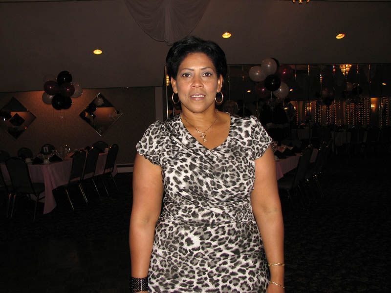 Woman in patterned dress stands in a banquet hall with balloons and tables.